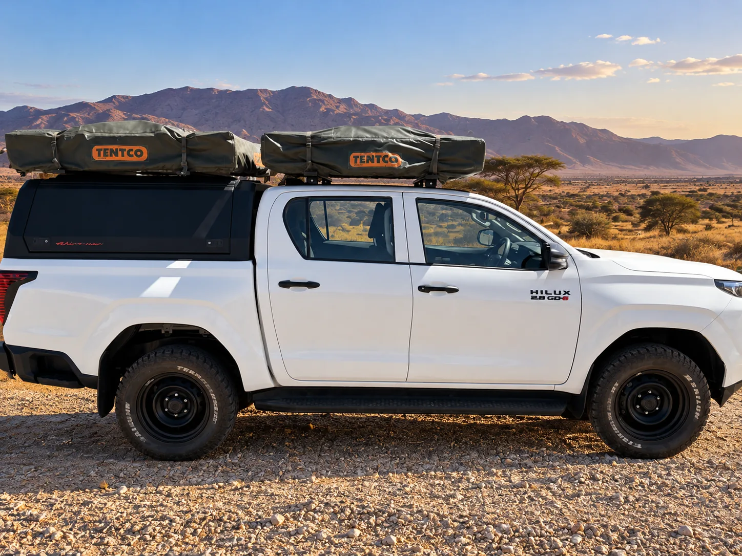White Toyota Hilux double cab with two folded rooftop tents, side view, in savanna