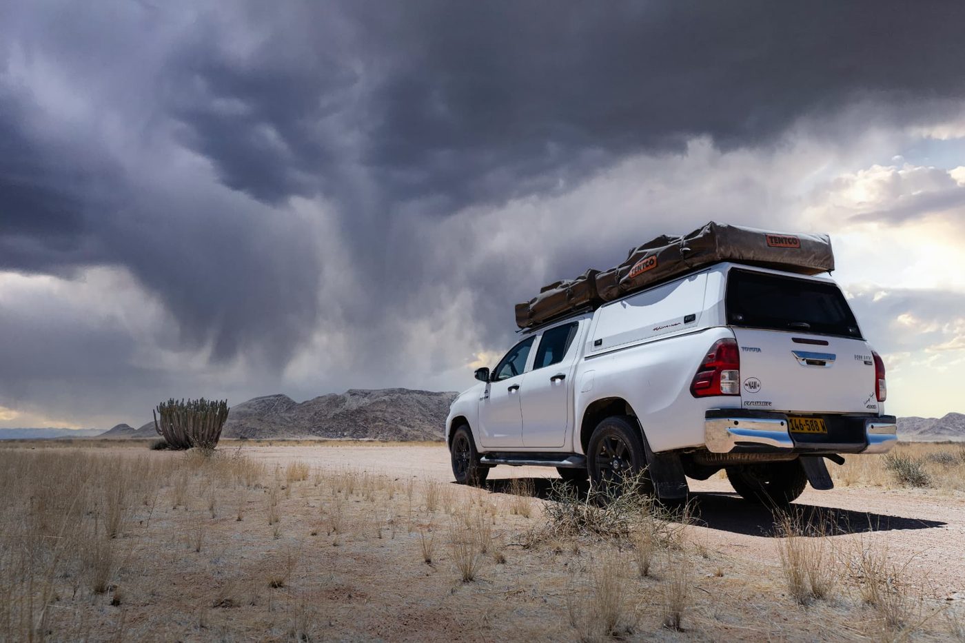 White Toyota Hilux Raider 4x4 with rooftop tents parked on a Namibian plain under dramatic storm clouds