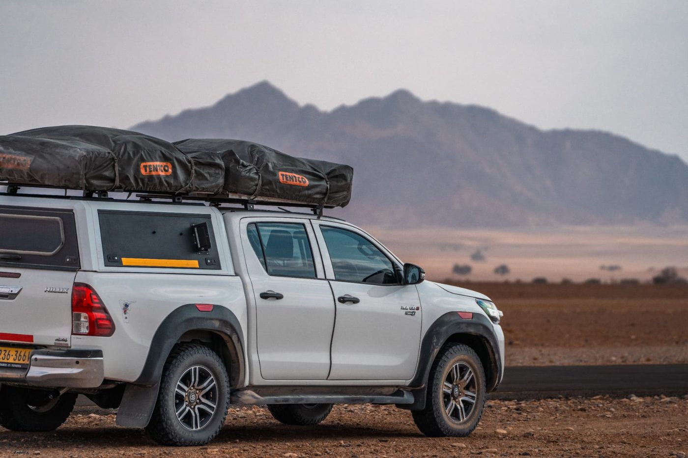 Toyota Hilux 2.4 Double Cab 4x4 with a single rooftop tent closed on the roof rack, on a Namibian gravel road
