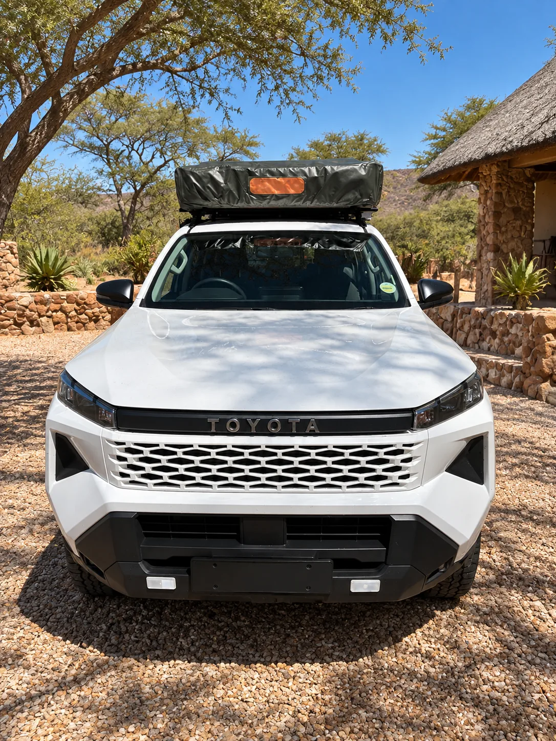 White Toyota Hilux with one folded rooftop tent, head-on view, at a lodge