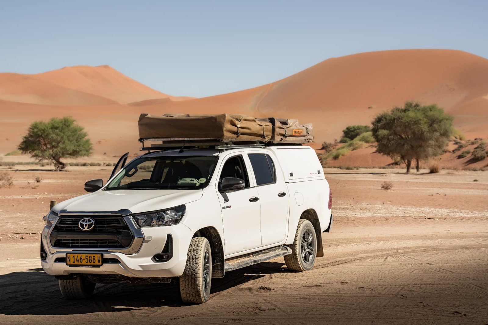 White Toyota Hilux Raider 2.4 Double Cab 4x4 rental with canopy, parked on a Namibian gravel road