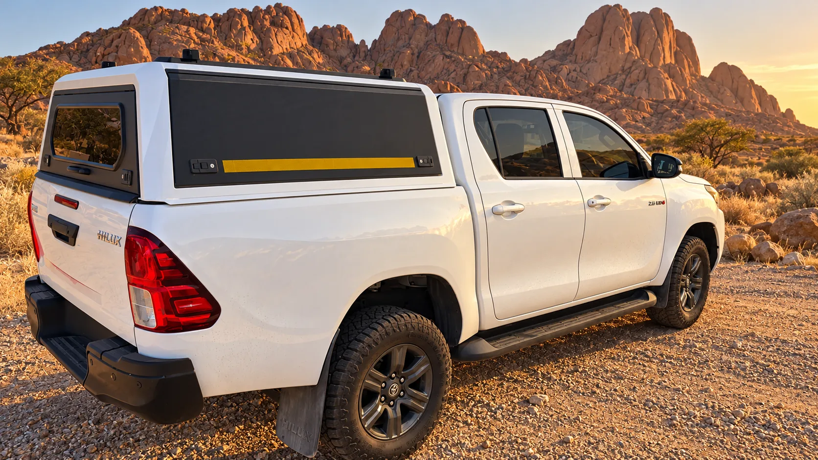 White Toyota Hilux double cab with canopy and no rooftop tent, rear three-quarter view, in a granite landscape