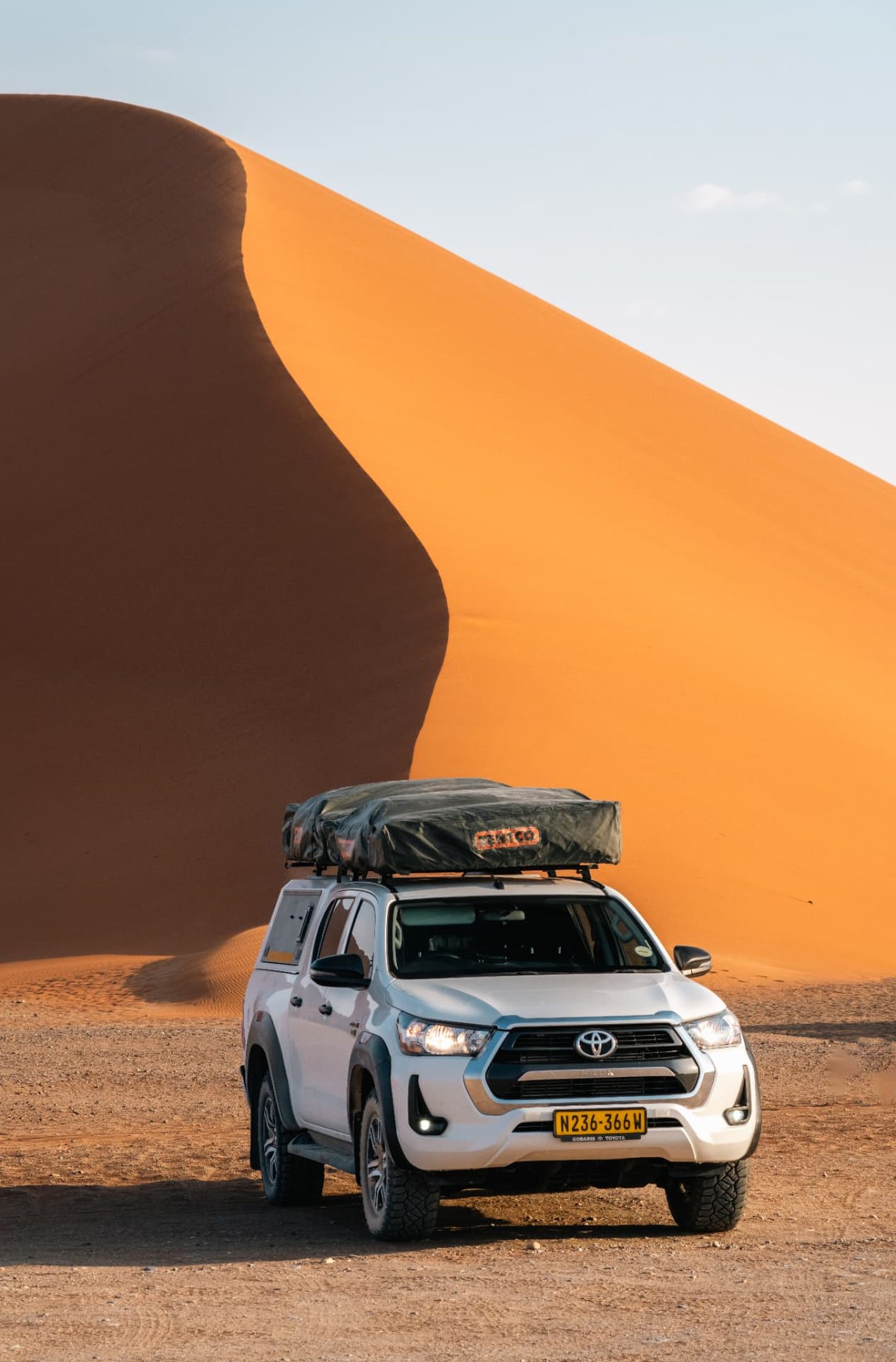 Toyota Hilux 4x4 with two rooftop tents closed on the roof rack in front of a red Sossusvlei dune